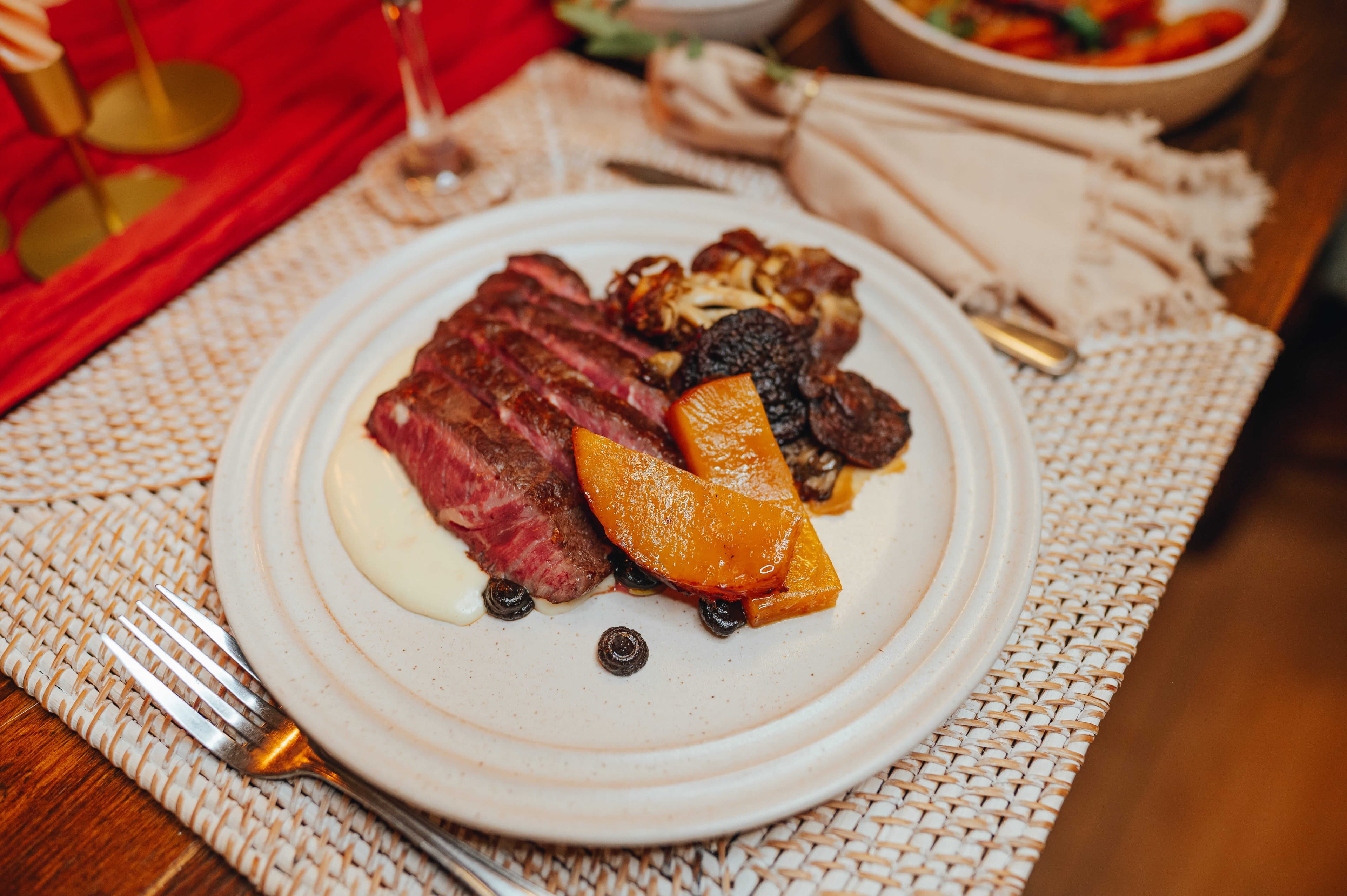 A plate of sliced steak accompanied by roasted vegetables and a creamy sauce.