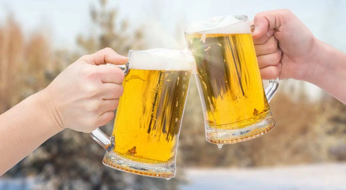 Two hands clink beer mugs against a winter backdrop.