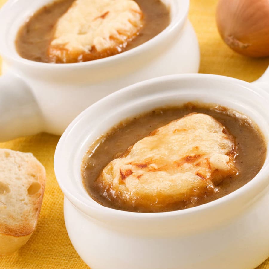 Two bowls of onion soup topped with melted cheese, accompanied by a slice of bread.