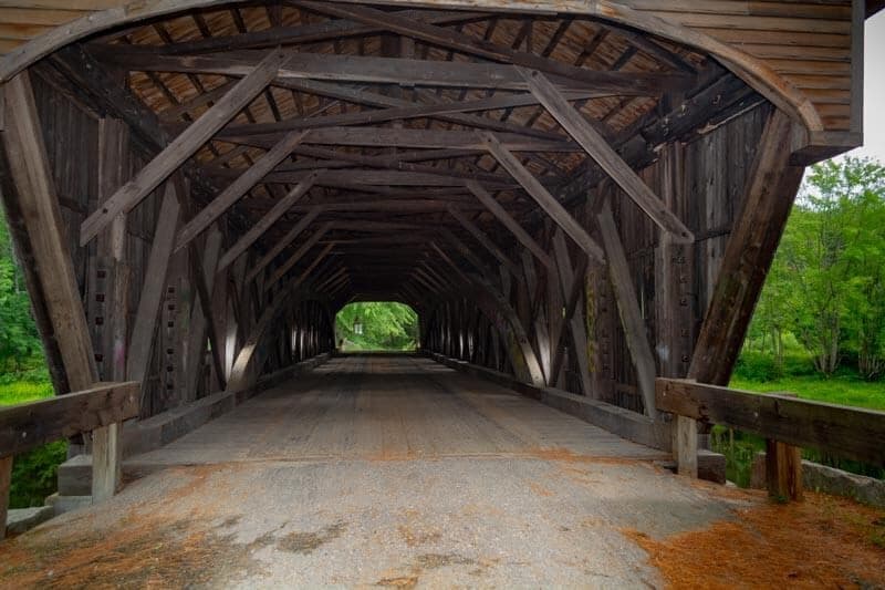 View of the interior of a wooden covered bridge leading to greenery.