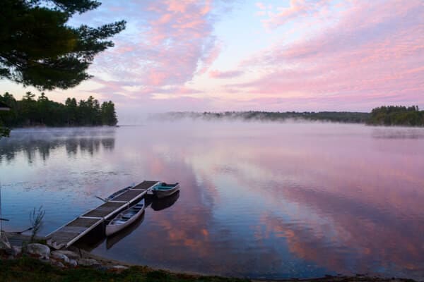 Serene lake at sunrise with fog and colorful clouds reflecting on the water.