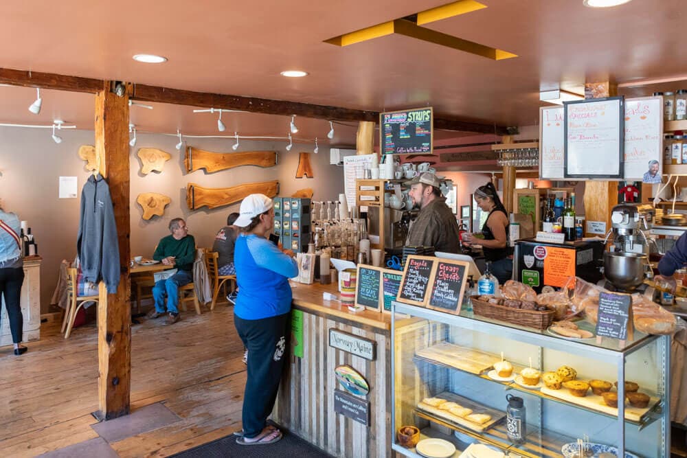 A cozy café interior featuring a counter with food displays, wooden accents, and patrons enjoying their time.