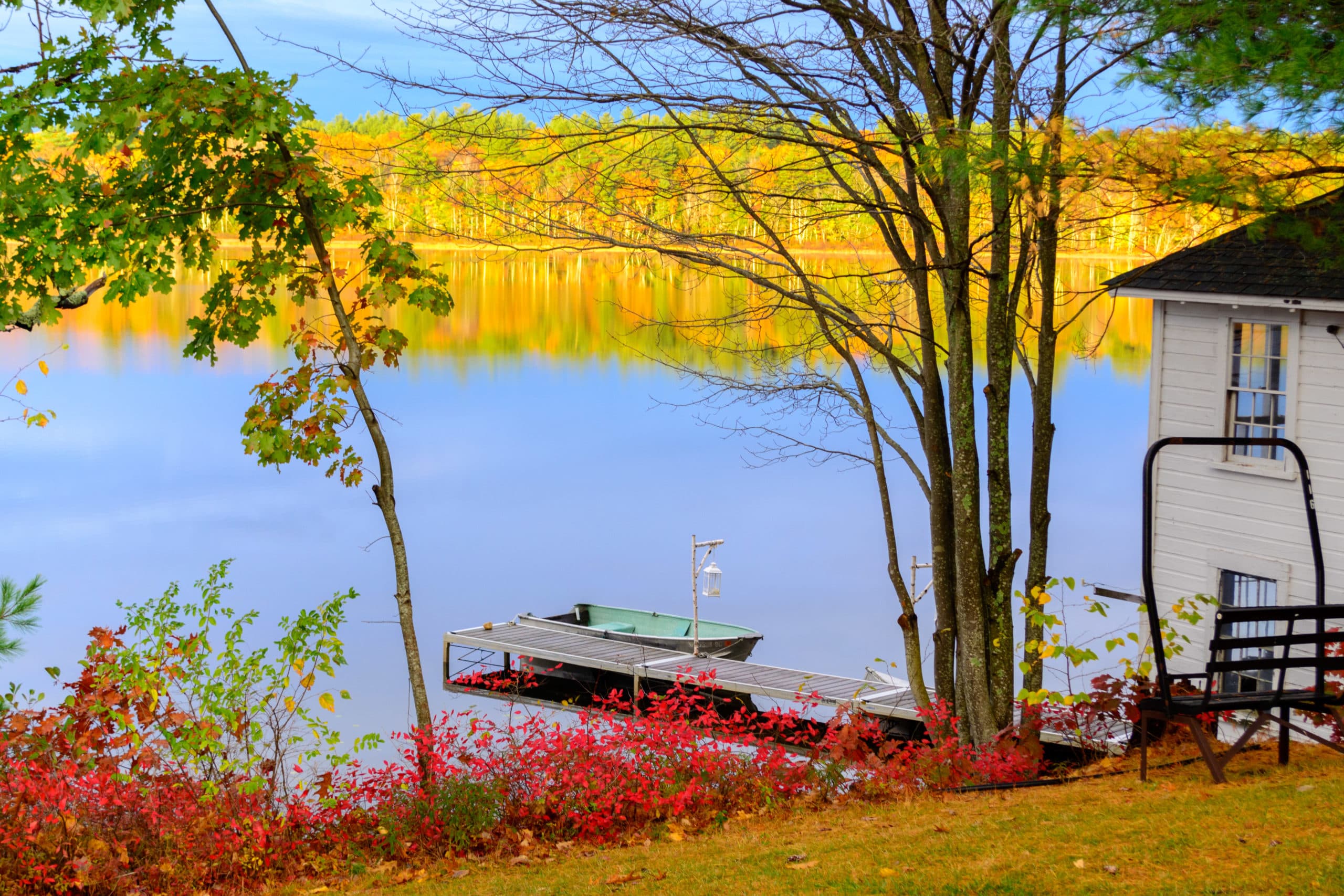 Scenic view of a calm lake with autumn foliage, a boat dock, and a house nearby.