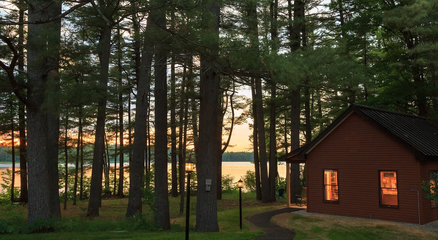 A cabin is nestled among tall trees by a lake at sunset. A cabin is nestled among tall trees by a lake at sunset.