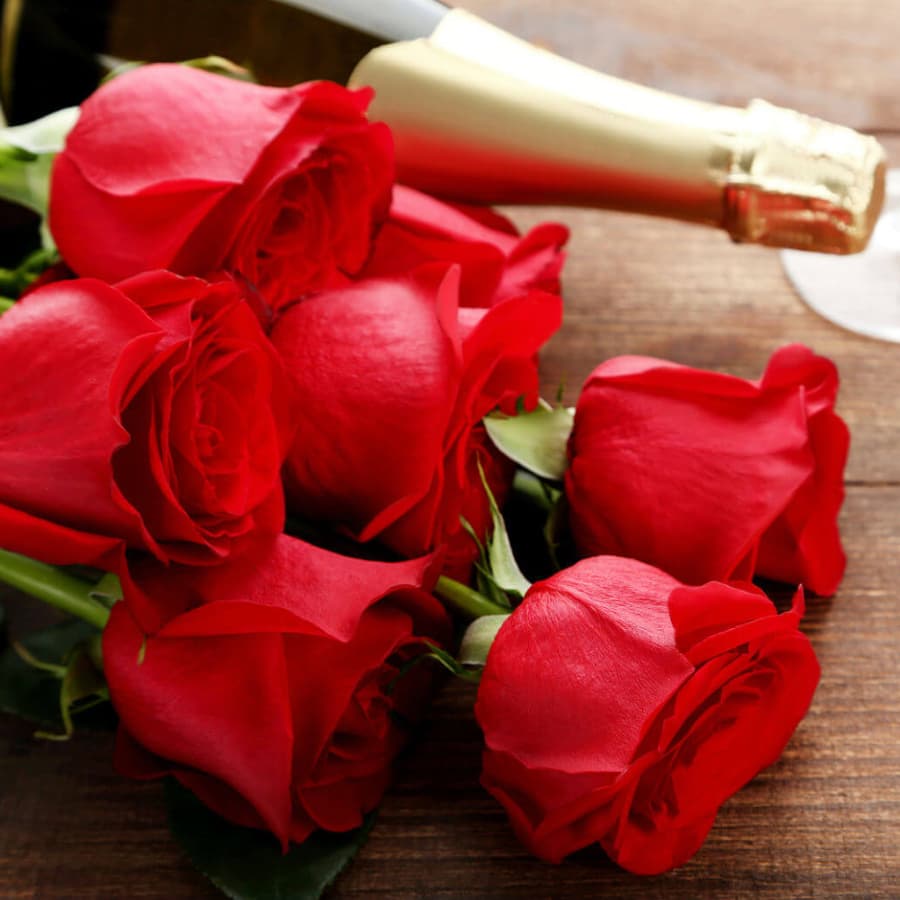 A bouquet of red roses with a bottle of champagne on a wooden surface.