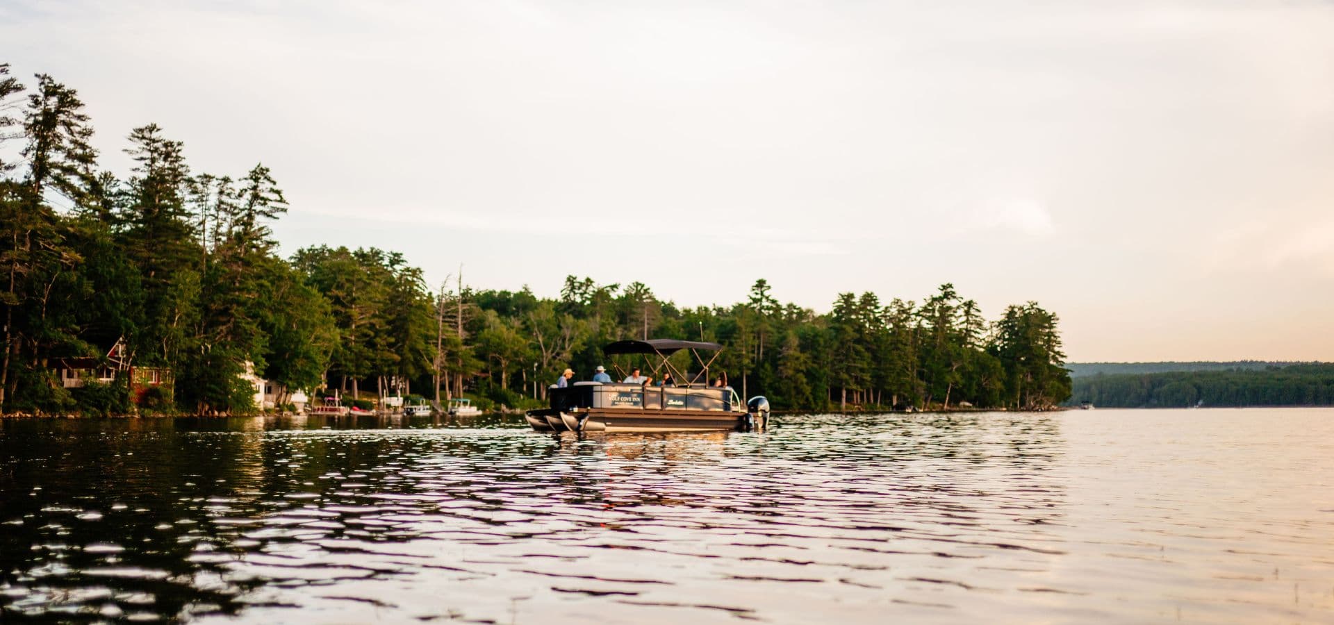 A boat gently glides across a calm lake surrounded by lush trees at dusk.