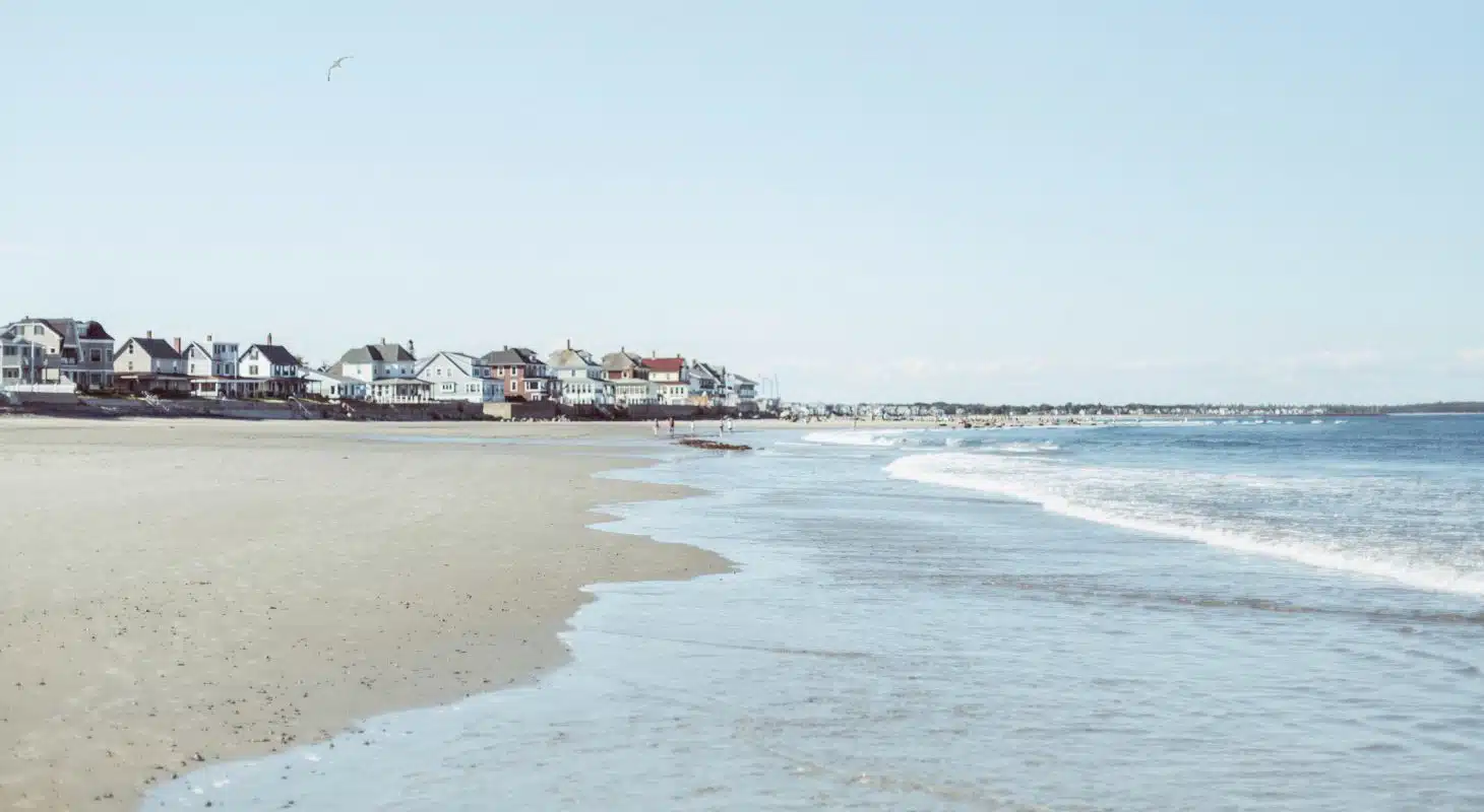 Coastal view with sandy beach and houses lining the shore under a clear blue sky.