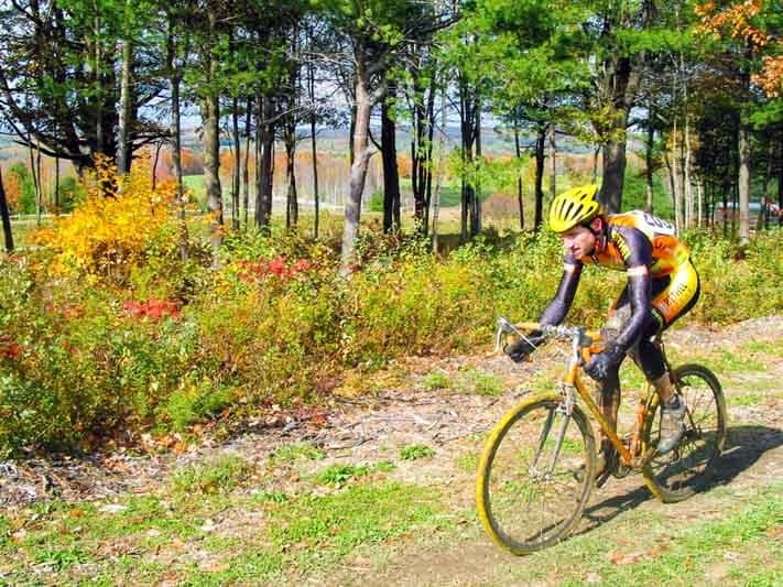 A cyclist navigates a muddy trail surrounded by autumn foliage.