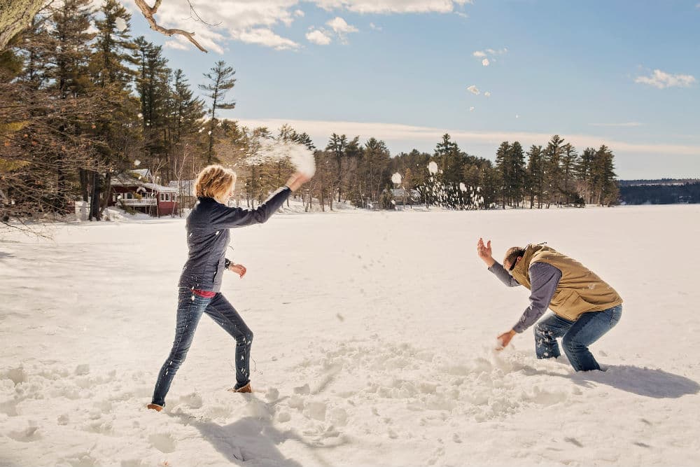 Two people play in the snow by throwing snowballs at each other on a sunny winter day.