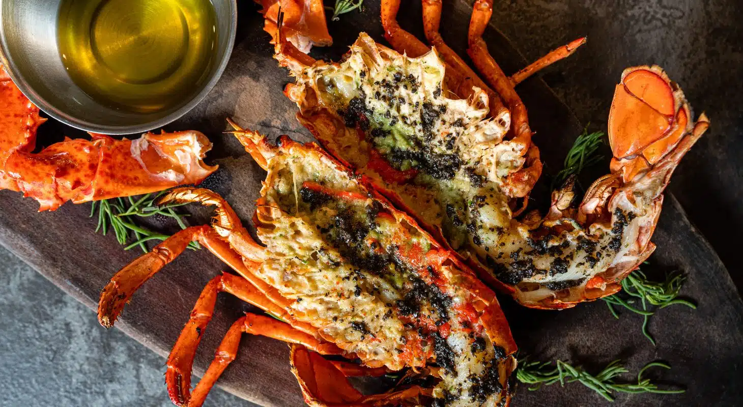 Grilled lobster served with herbs and a bowl of olive oil.