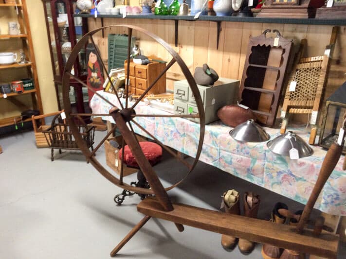 A wooden spinning wheel is displayed alongside various vintage items in an antique shop.
