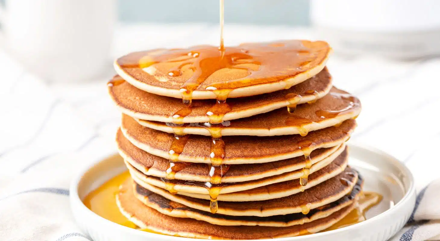 A tall stack of pancakes with syrup cascading down.