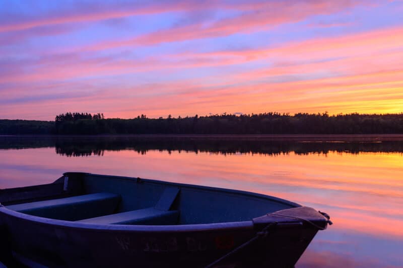 A small boat on still water reflects a vibrant sunset of pink and purple hues.