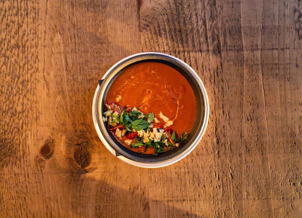 A bowl of tomato soup garnished with herbs and spices, placed on a wooden table.