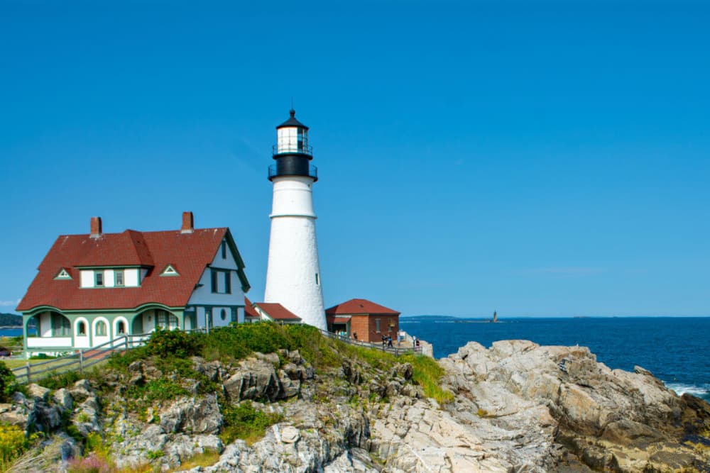 Lighthouse beside a rocky shore with a blue sky in the background.