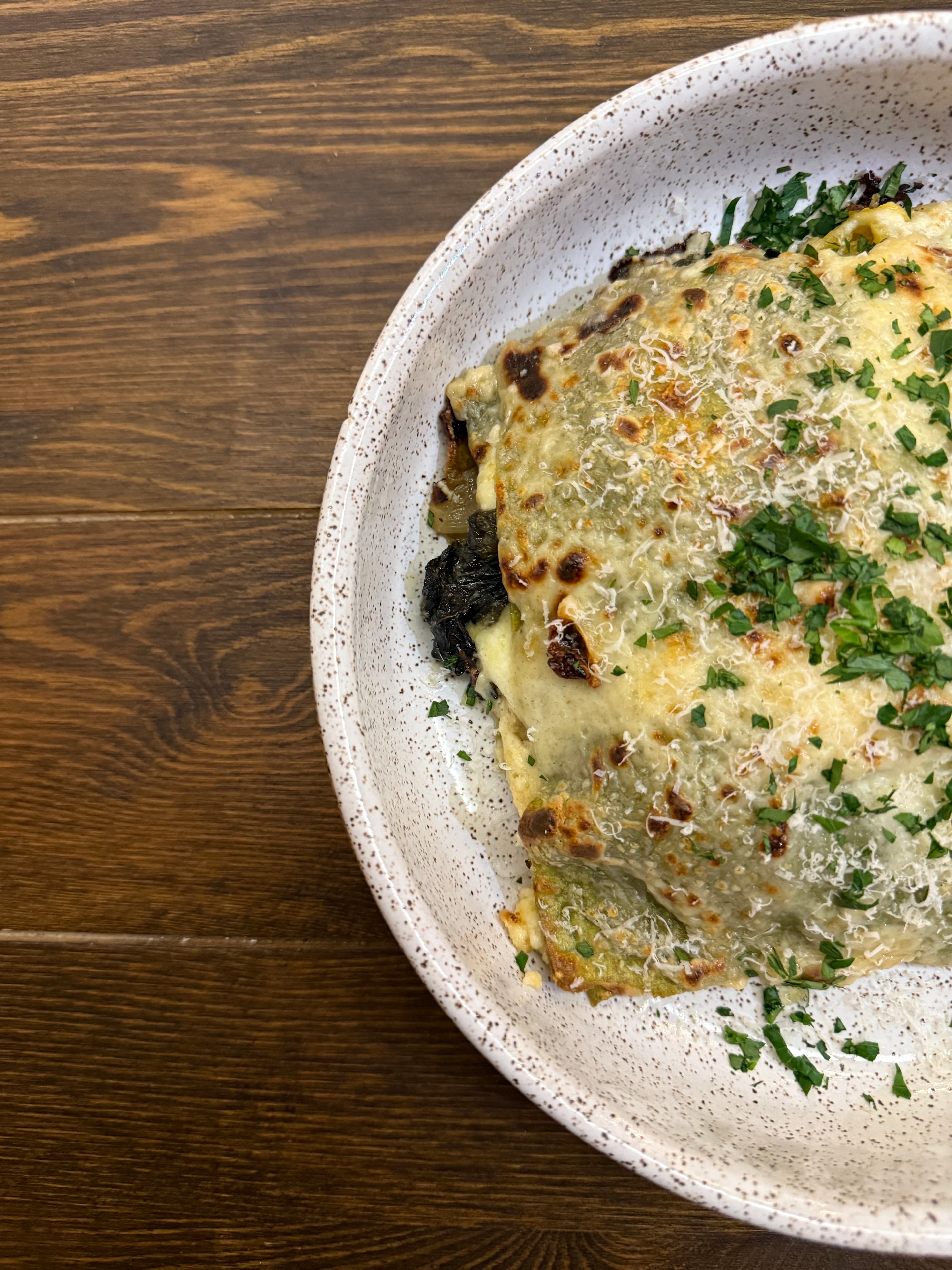 A portion of lasagna topped with melted cheese and garnished with fresh herbs in a speckled bowl.