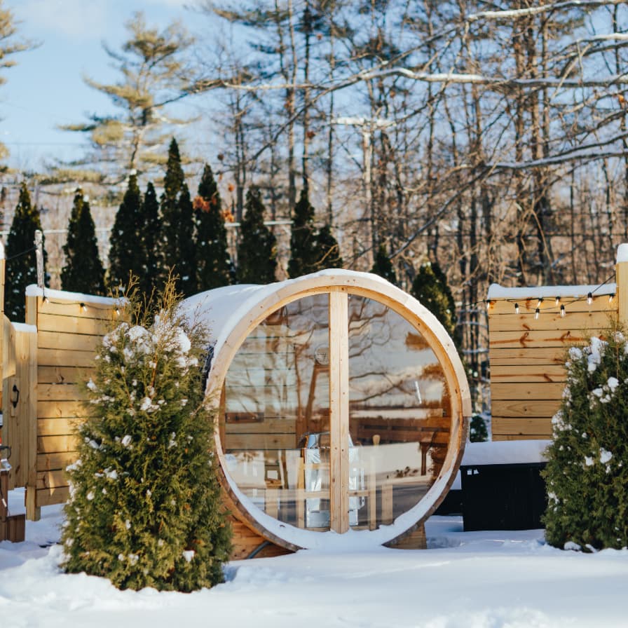 A circular wooden structure sits surrounded by snow and evergreen trees.