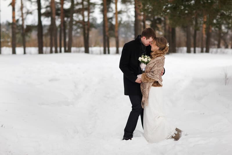 A couple in winter attire shares a romantic kiss among snowy trees.