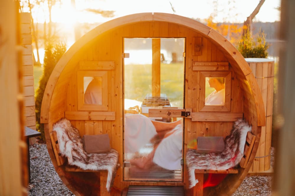 A wooden sauna cabin with two people relaxing inside at sunset.