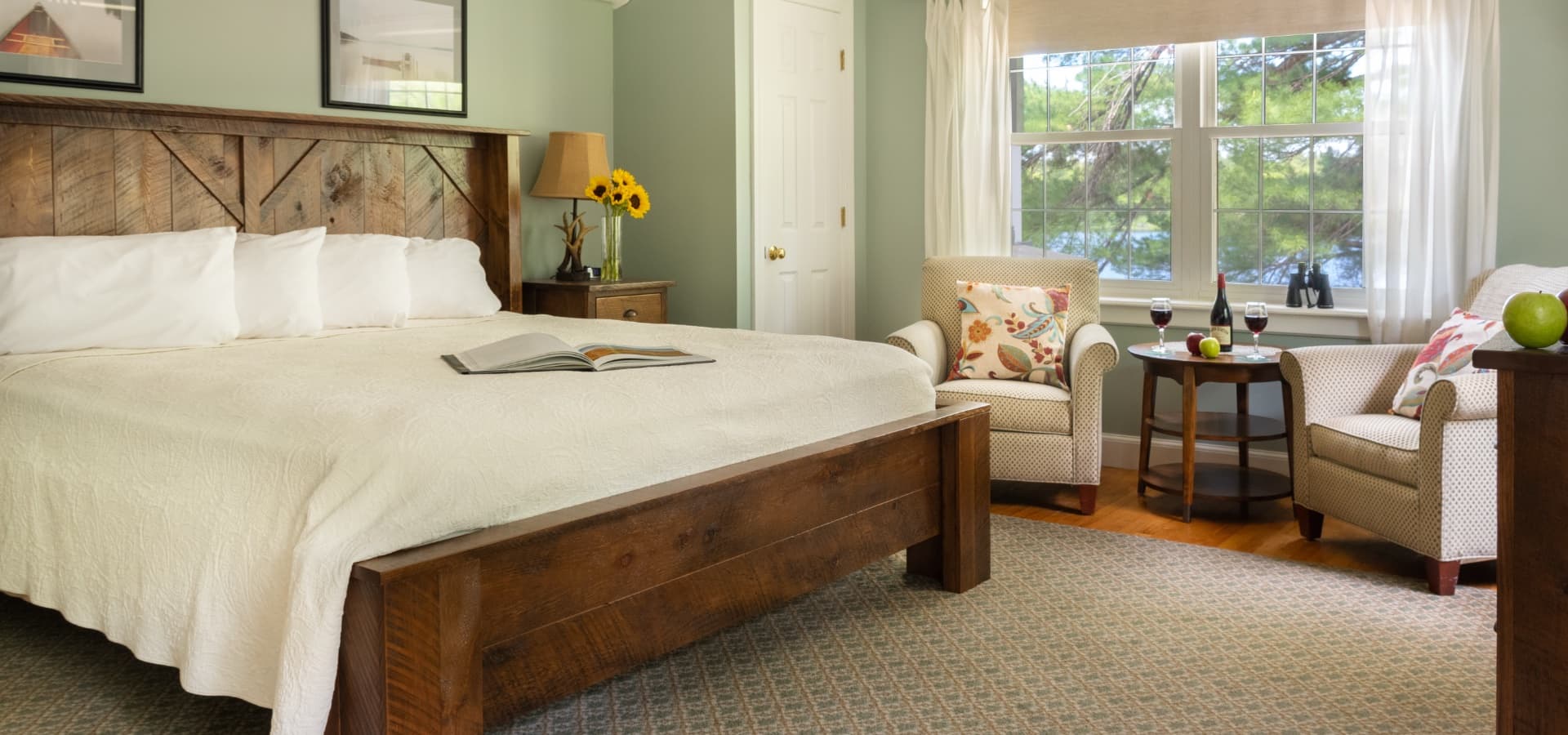 Cozy bedroom featuring a wooden bed, armchairs, and a window with natural light.