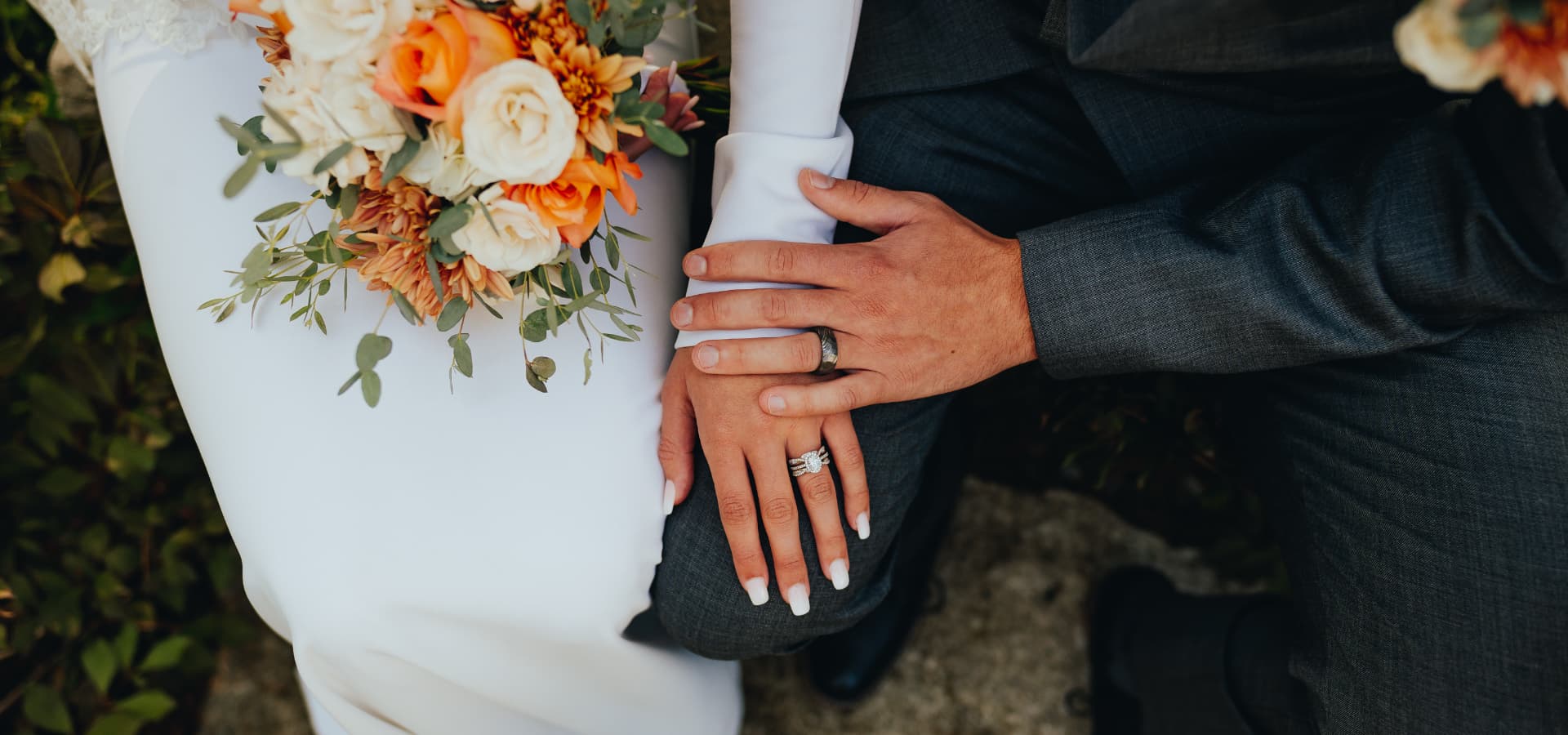 A close-up of a bride's and groom's hands intertwined, showcasing wedding rings and a bouquet.