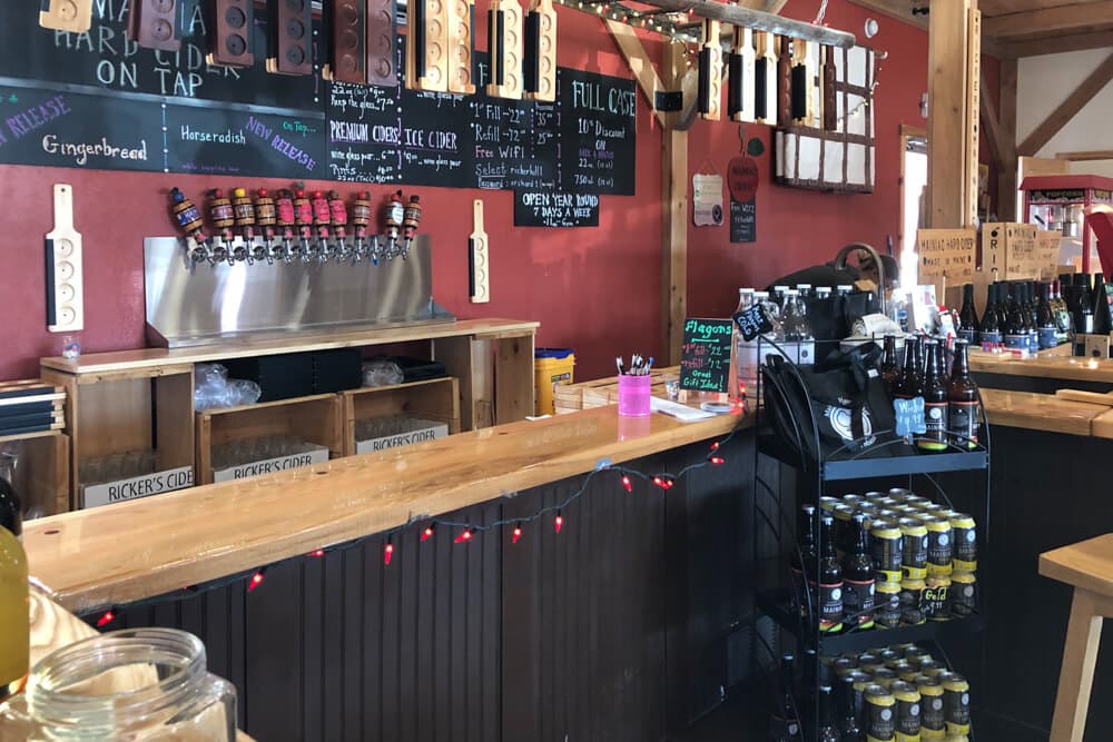 A cozy bar with a wooden counter, several taps for drinks, and shelves stocked with various beverages.