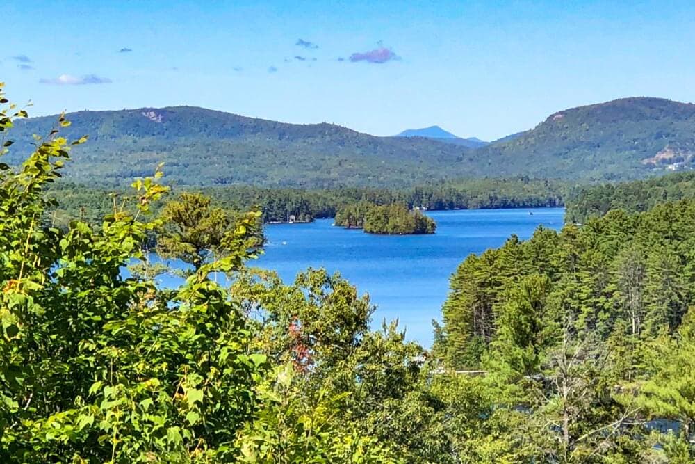 A serene lake surrounded by green forests and hills under a clear blue sky.
