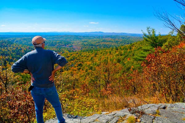 A person stands on a rock, gazing at a colorful autumn landscape.