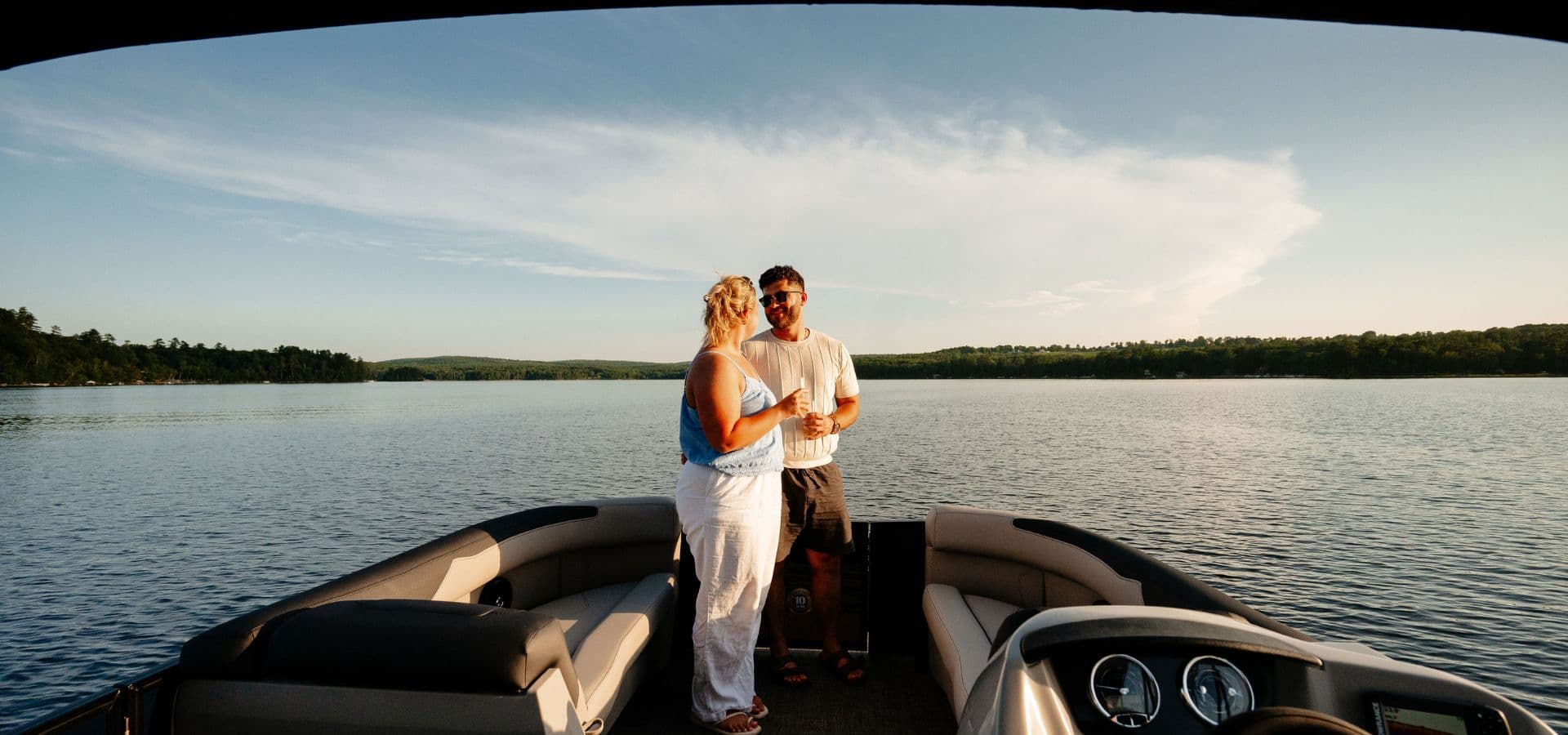 A couple enjoys a romantic moment on a boat while overlooking a calm lake at sunset.