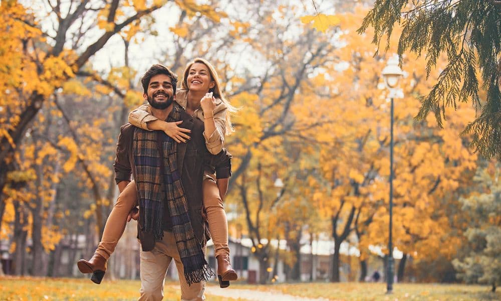 A smiling couple enjoying an autumn day in a park surrounded by golden fall leaves.