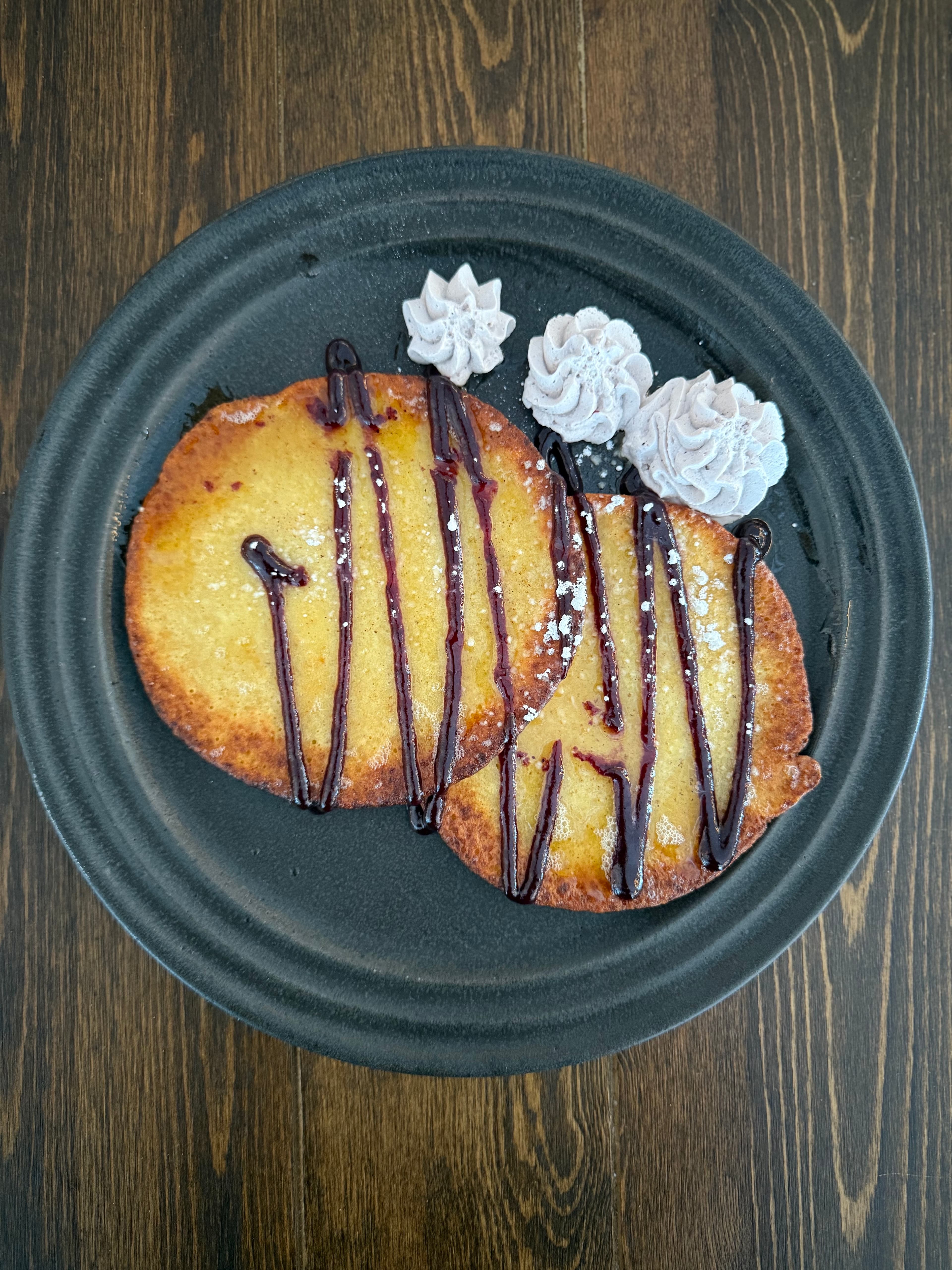 A plate with two golden pancakes drizzled with chocolate sauce and garnished with swirls of whipped cream.