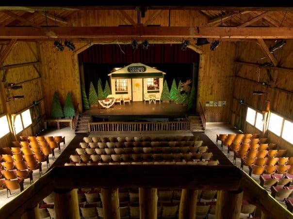 Interior of a rustic theater with empty seats facing a wooden stage set.