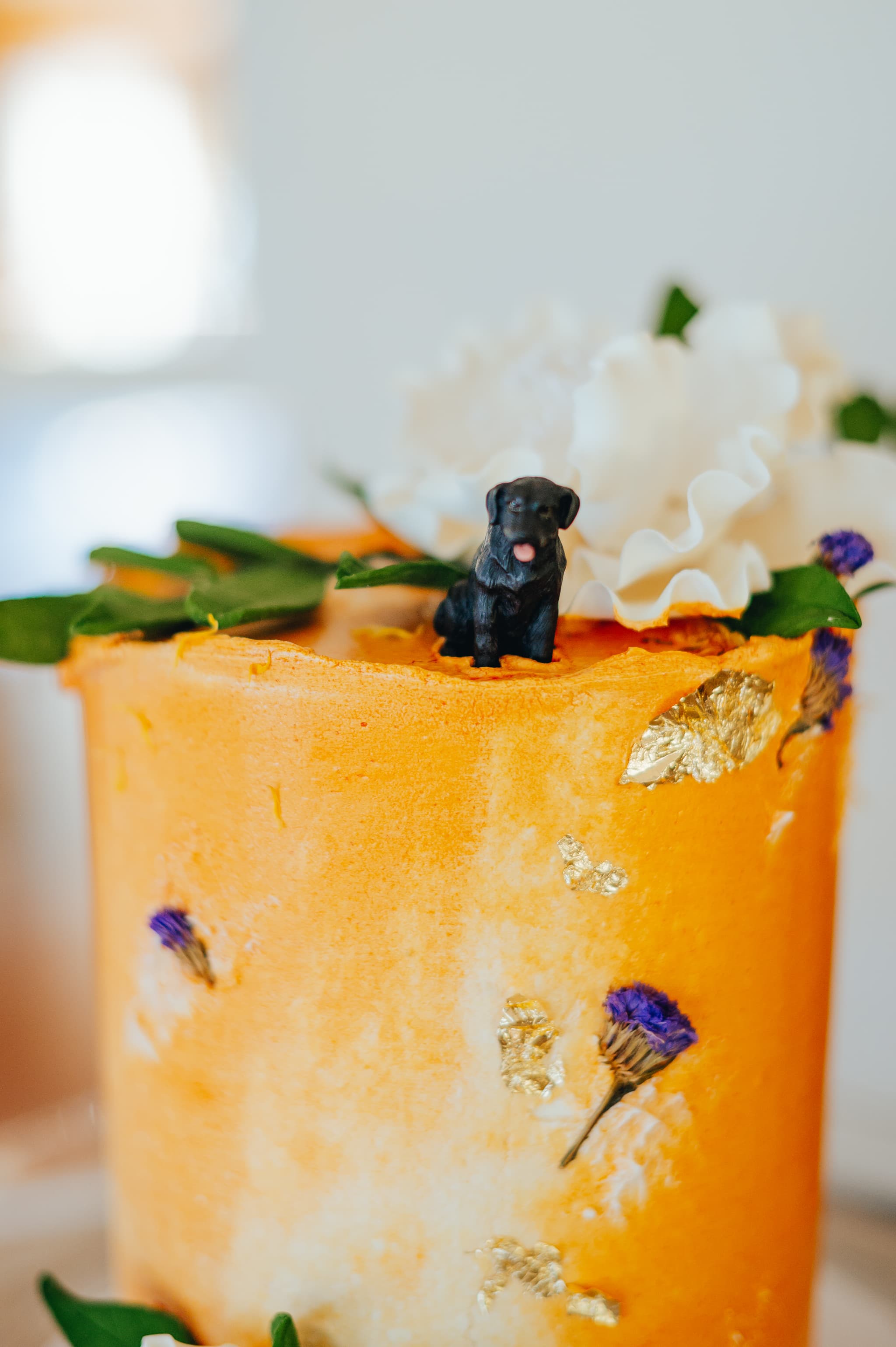 A decorative orange cake topped with a small black dog figurine and white flowers.