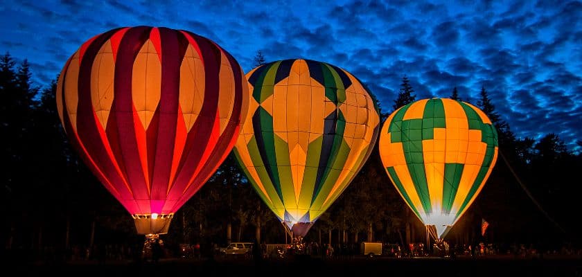 Three illuminated hot air balloons glowing against a twilight sky.