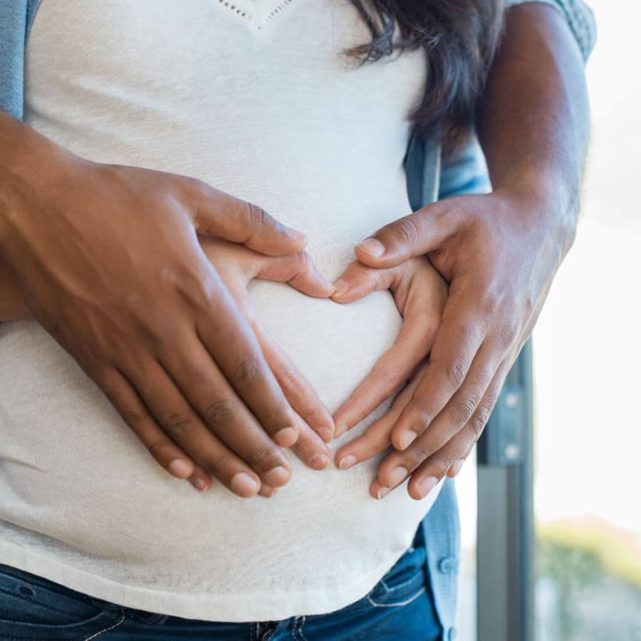 Two hands forming a heart shape on a pregnant belly.