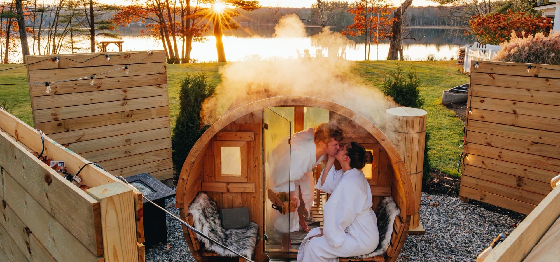 A couple shares a kiss inside a steaming wooden sauna, set against a backdrop of a lake and sunrise.
