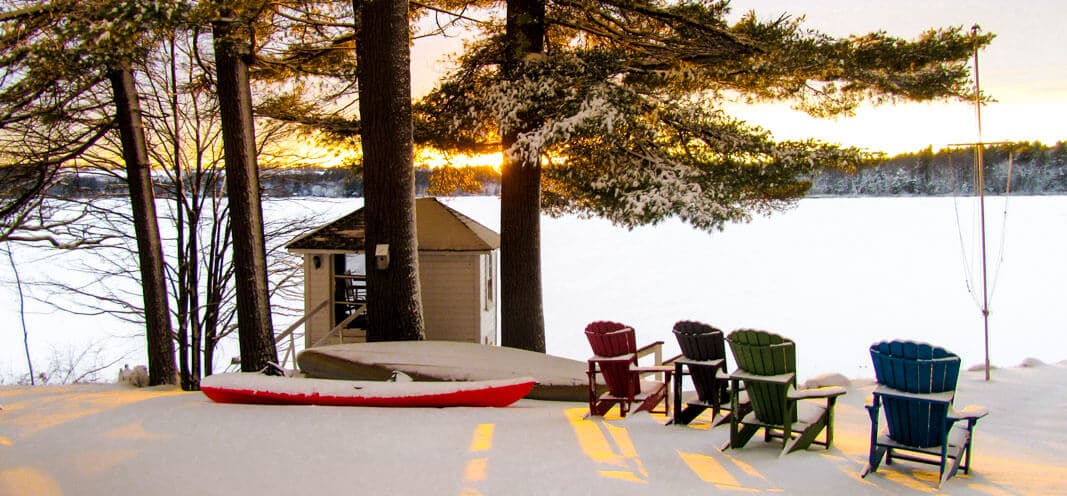 A cozy lakeside scene at sunset, featuring colorful chairs and a snow-covered shoreline.