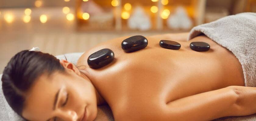 A woman relaxes on a massage table with hot stones placed on her back.
