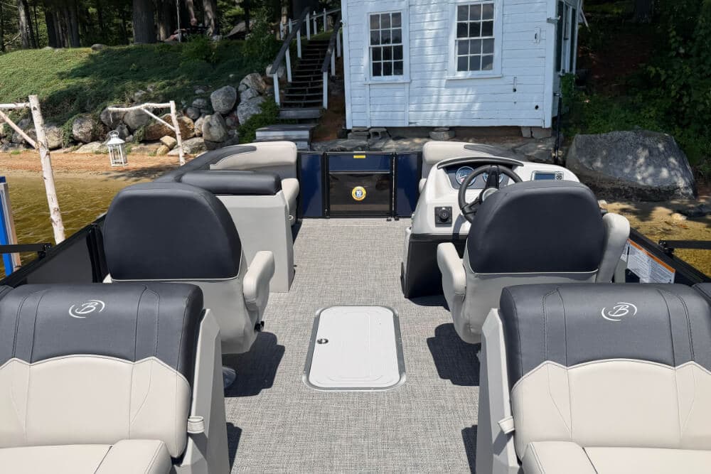 Interior view of a spacious boat with two facing seats and a steering console, set against a lakeside backdrop.