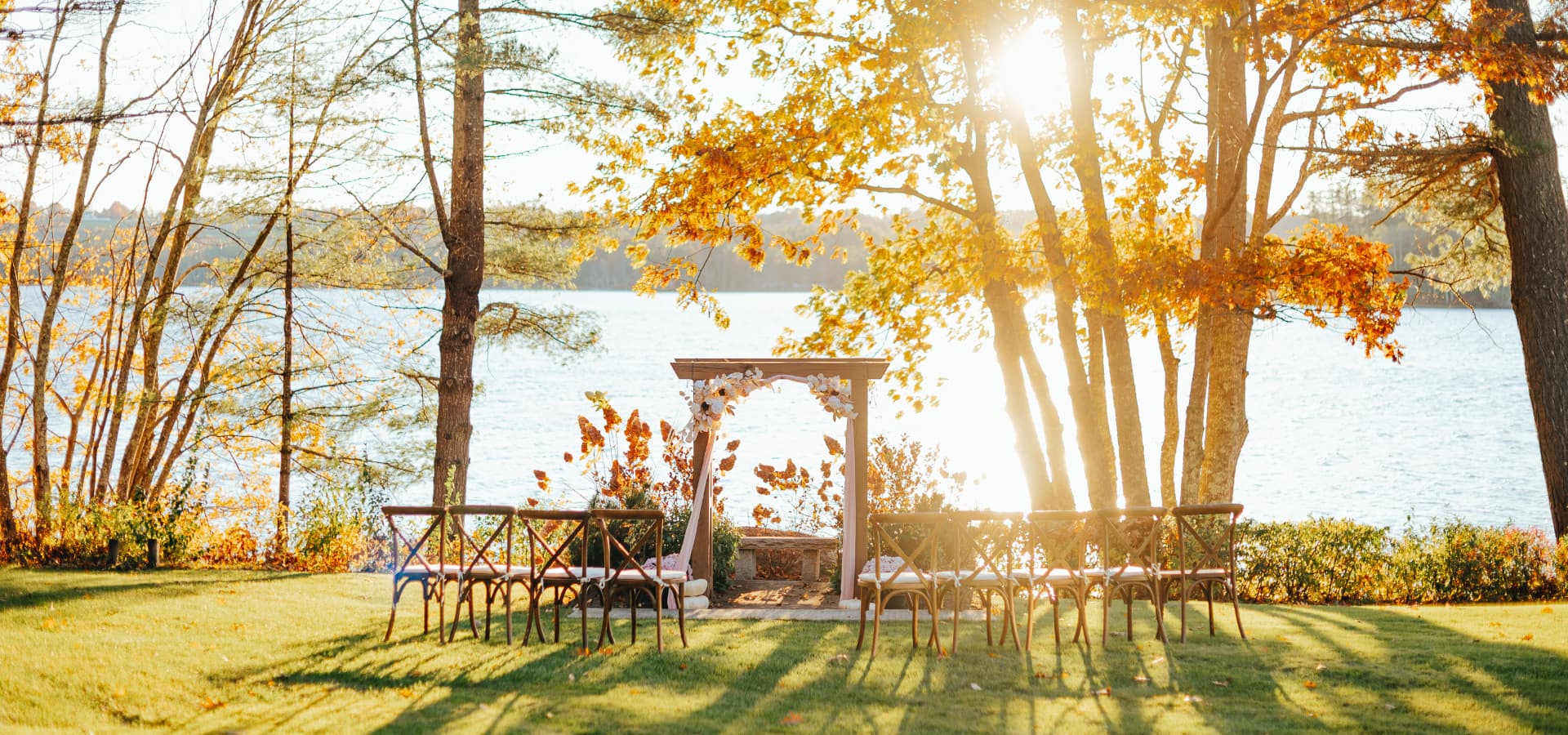 A waterfront wedding venue adorned with autumn foliage and empty chairs arranged for guests.