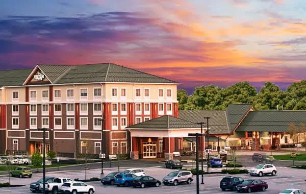 A hotel building at sunset with cars parked in the foreground.