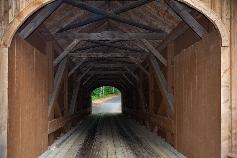 View of the interior of a wooden covered bridge, leading to a pathway.
