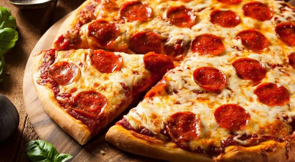 A freshly baked pepperoni pizza on a wooden cutting board with one slice removed.