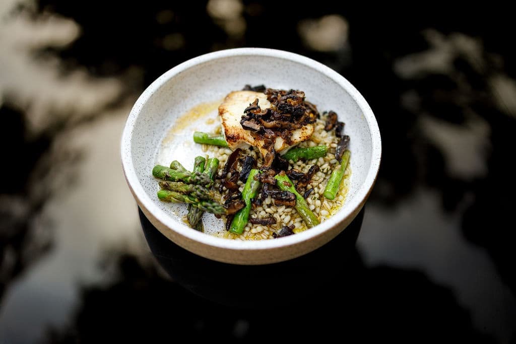A bowl of grilled fish served with asparagus and a savory sauce over a bed of grains.