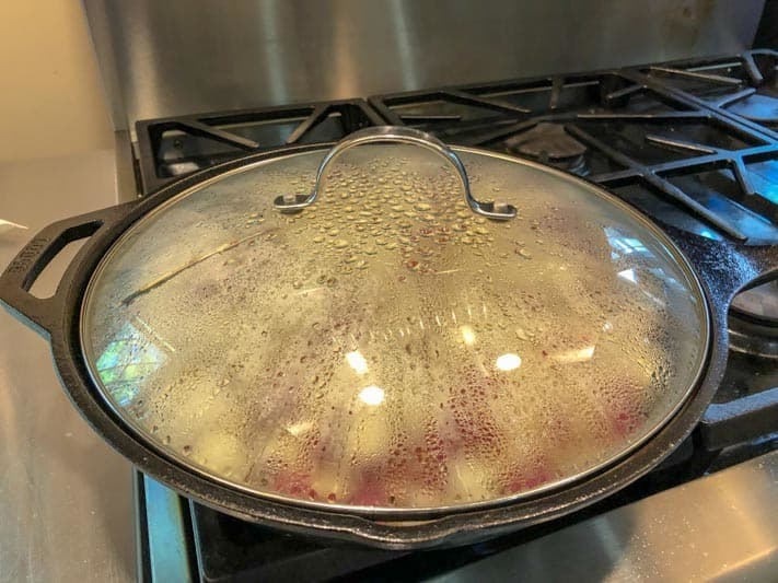 A pot with a glass lid covered in condensation sits on a stovetop.