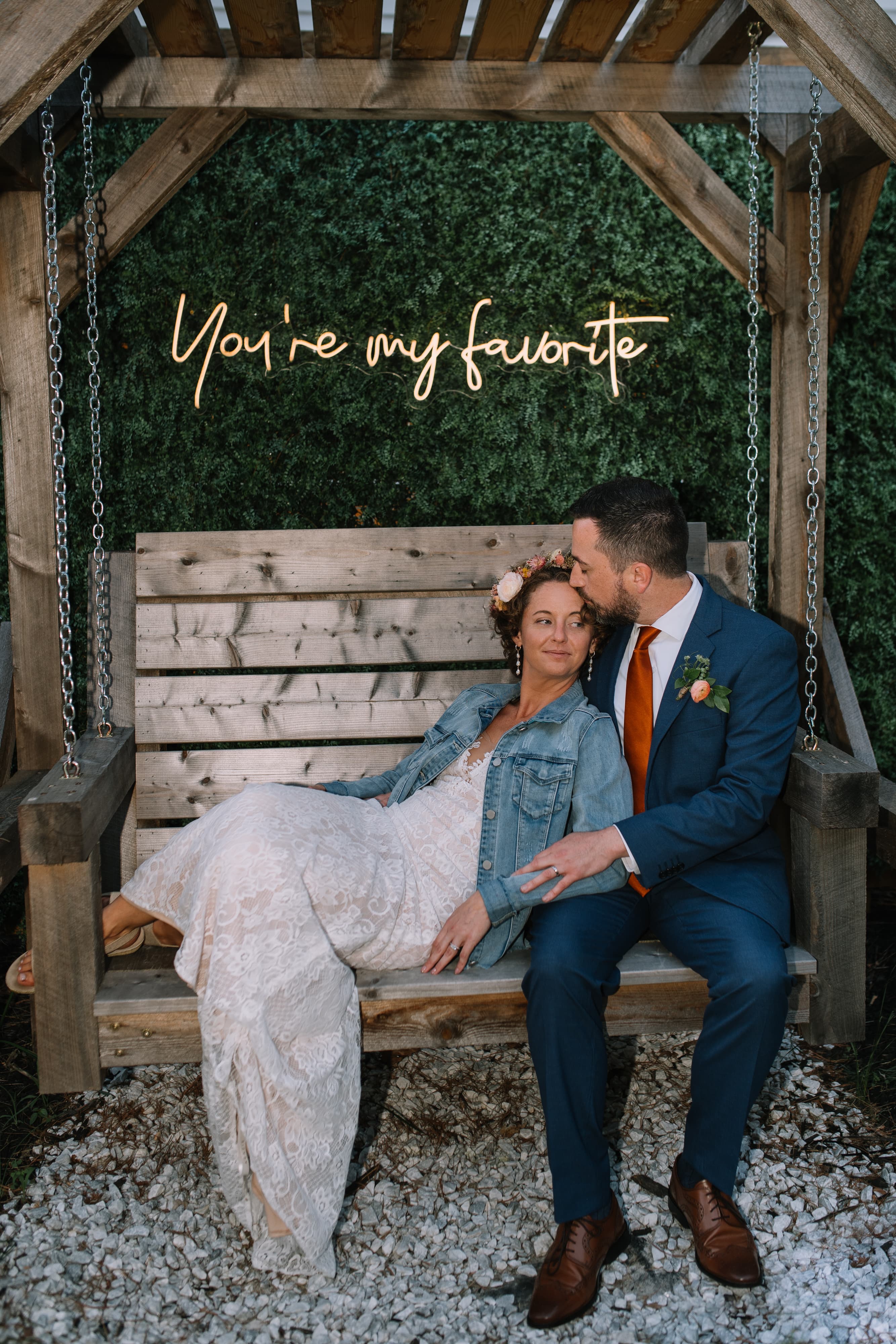 A couple sits together on a wooden swing, surrounded by greenery, with a glowing sign that reads, "You're my favorite."