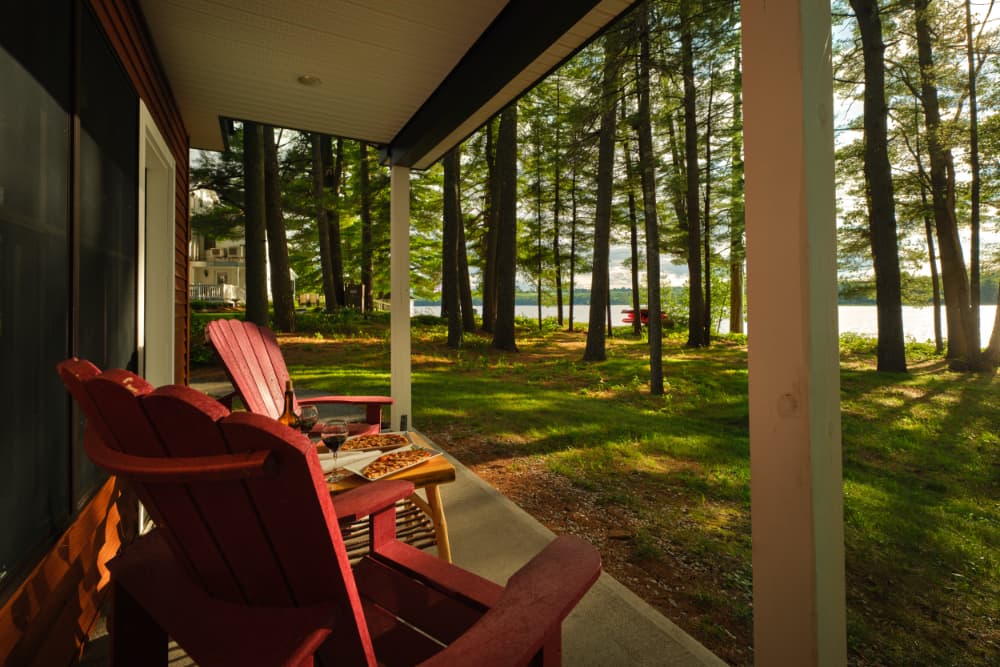 A cozy porch with red chairs overlooks a serene lakeside surrounded by trees.
