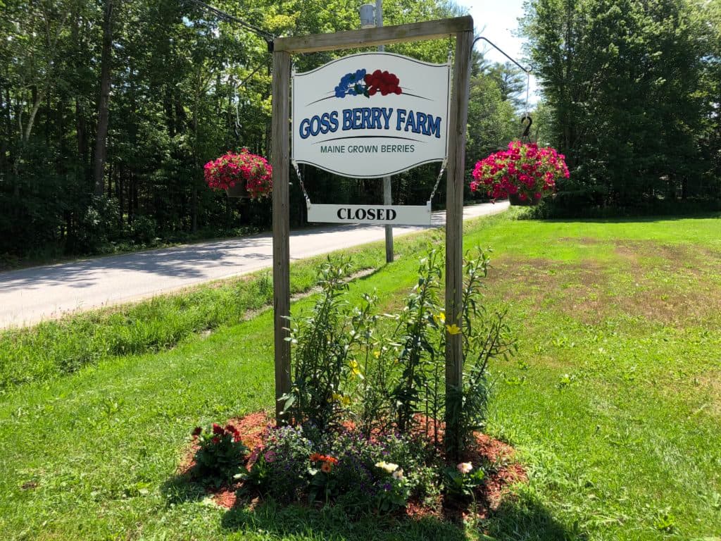 Sign for Goss Berry Farm, indicating it is closed, surrounded by greenery and flowers.
