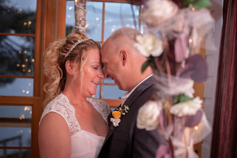 A happy couple shares a tender moment during their wedding, framed by flowers and soft lighting.