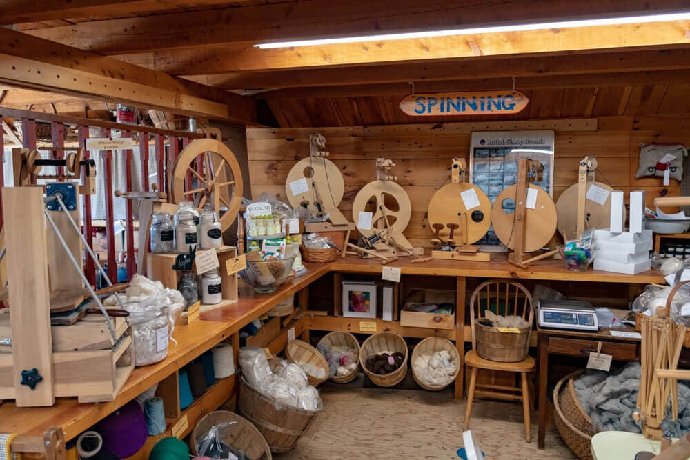 A cozy workshop filled with spinning wheels, fibers, and crafting supplies.